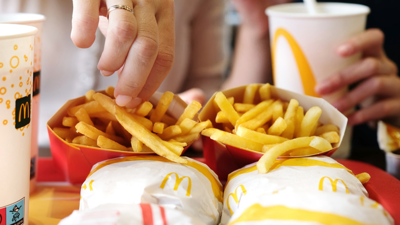 A hand grabs a french fry from a McDonald's tray filled with sandwiches, drinks, and fries.