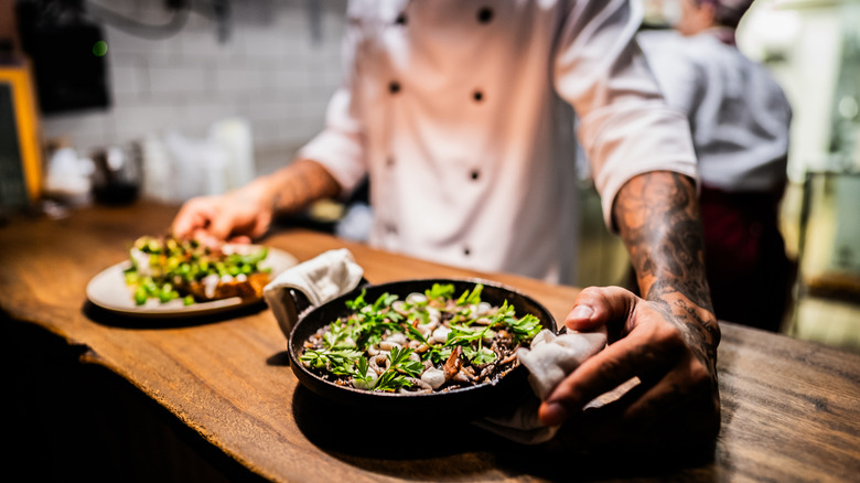 A chef with tattooed arms presents two dishes of food