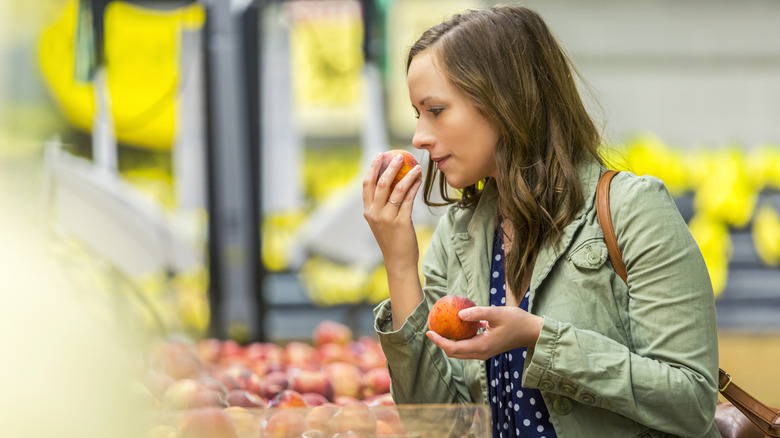Woman holding peach to her nose inside grocery store