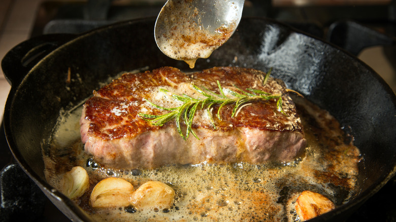 A thick-cut steak being basted with butter in the pan