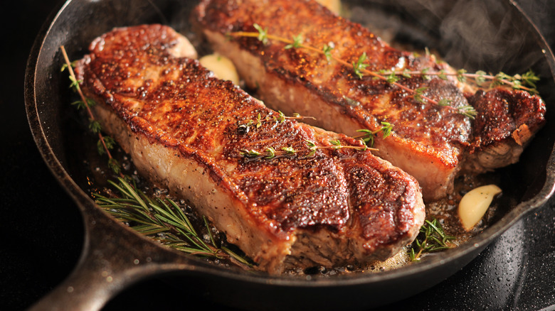 Two strip loins pan seared in a cast iron pan with herbs and garlic