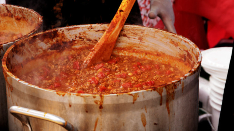 A large pot of chili being stirred with a wooden spoon as it cooks