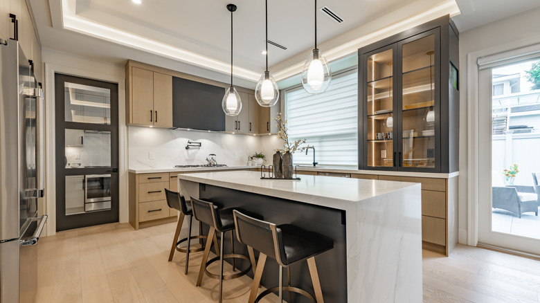 entertainer's kitchen with bar stools hanging lights and a waterfall countertop on island