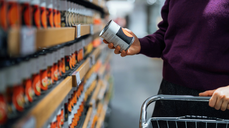 A person grabbing canned food from a grocery store shelf