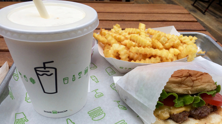 A Shake Shack branded parchment paper lined tray with a milkshake, french fries, and a cheeseburger.