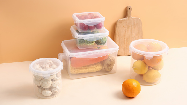 Variety of plastic food containers containing lemons, mushrooms, and other vegetables sitting on a kitchen counter