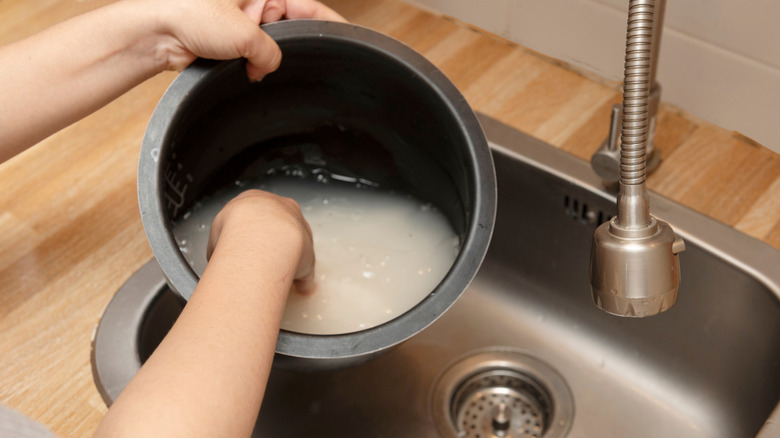 A person washing a pot of rice over a sink