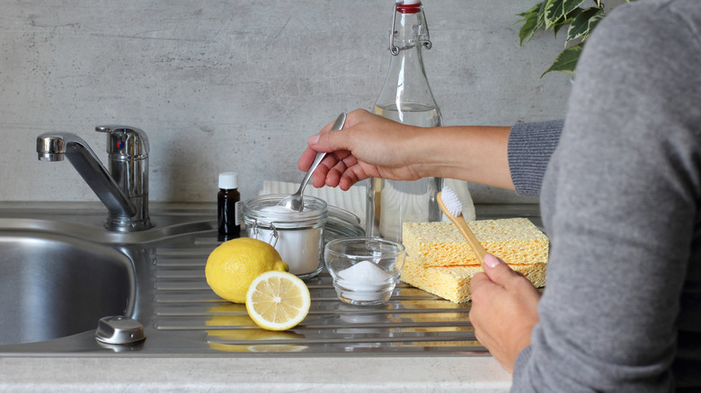 A woman getting ready to clean a kitchen sink with lemons, baking soda, and a brush