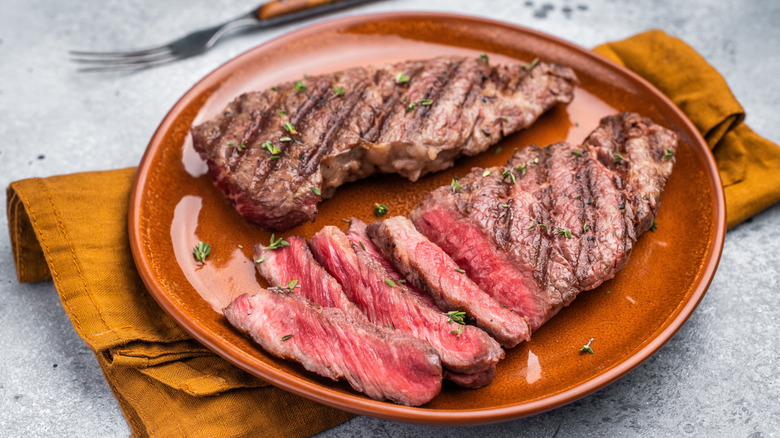 Two grilled flat iron steaks on a plate topped with a few herbs