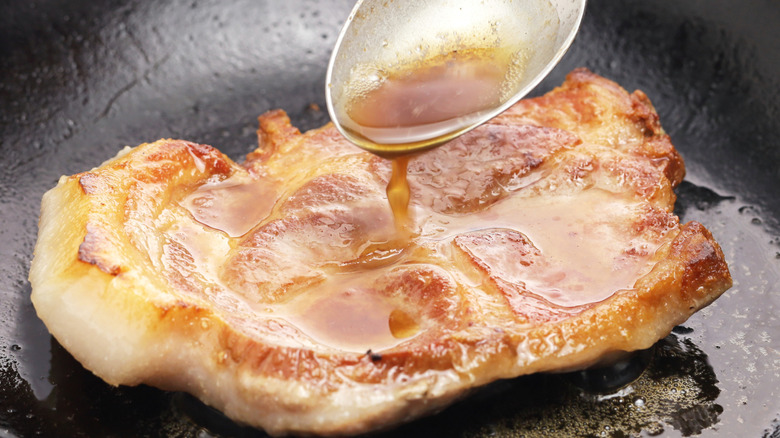 A pork chop is basted in a skillet