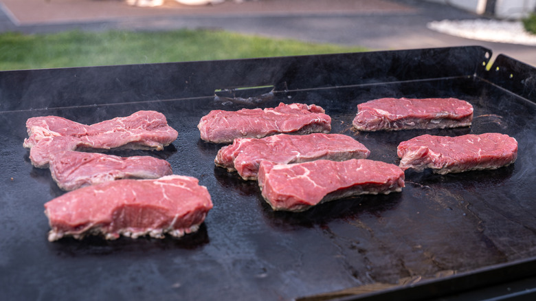 Steaks searing on an outdoor flat-top grill