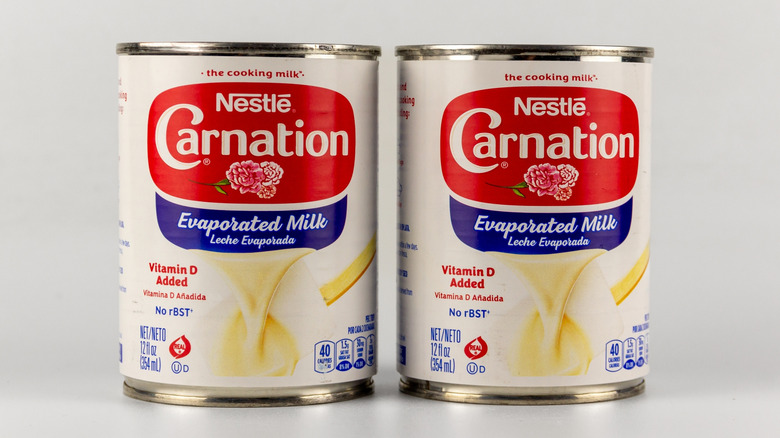 Two cans of Nestle Carnation Evaporated Milk against white background