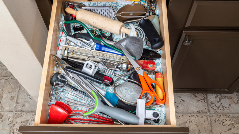 A kitchen junk drawer overflowing with kitchen tools, a pair of scissors and a rolling pin