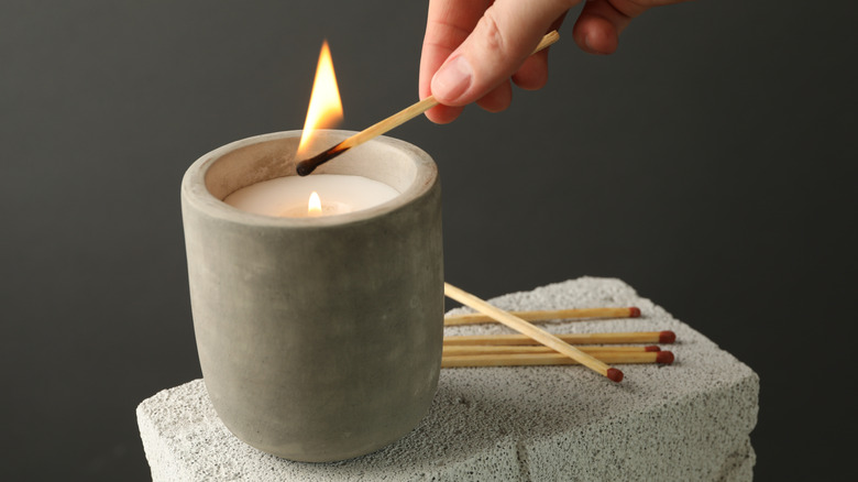 Woman lighting a candle with long match against gray background