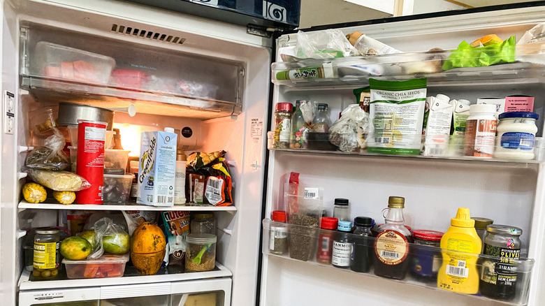 Messy interior of a refrigerator filled with fruits, vegetables, and other foods