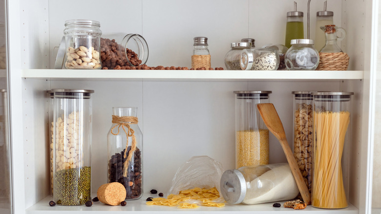 Cluttered kitchen cabinet shelves with various types of pastas, oils, and nuts