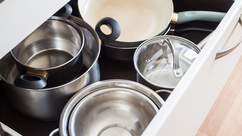 Open drawer of kitchen cabinet with steel pots, pans, and bowls