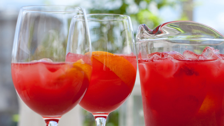 two wine glasses filled with a red cocktail beside a pitcher of the same