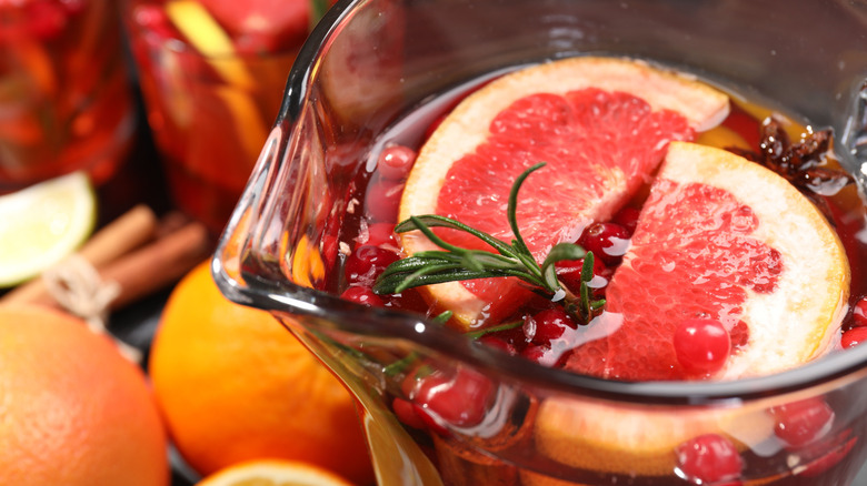 a pitcher of punch with grapefruit slices on top and a sprig of rosemary
