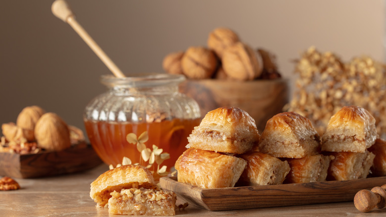 sliced baklava on a wooden tray with a large jar of honey in the background
