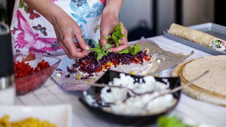 young woman in a colorful apron preparing burritos with fresh cheese and vegetables