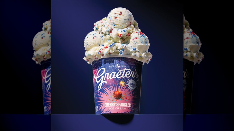 Pint of Graeter's Cherry Sparkler ice cream with scoops on top on blue background