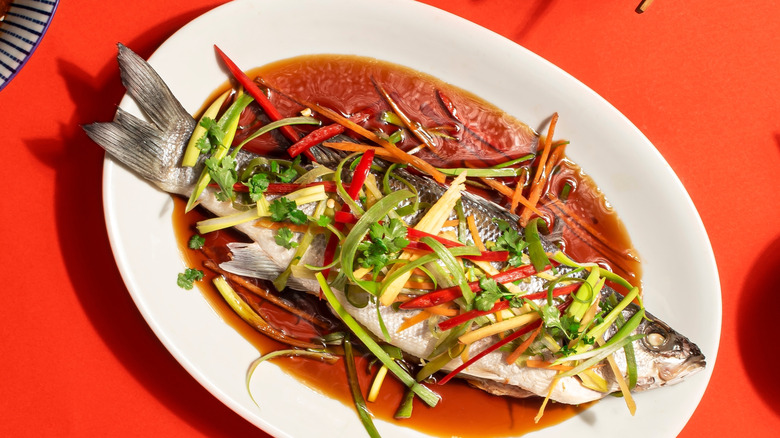 Aerial shot of a whole steamed fish on a plate with sliced vegetables