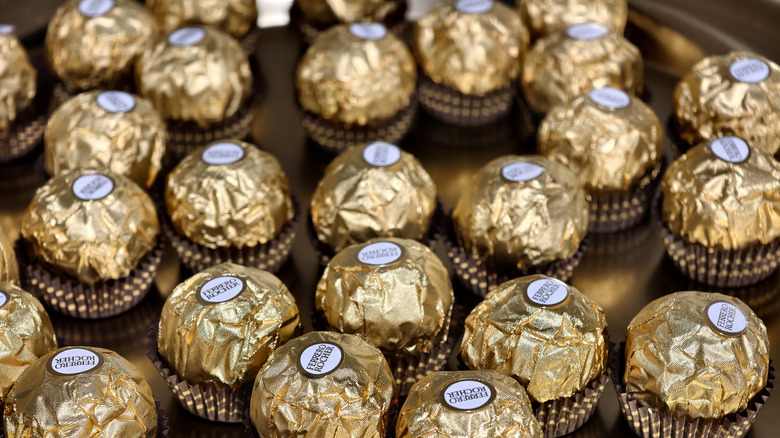 Lots of wrapped Ferrero Rocher candies sit on a gold table.
