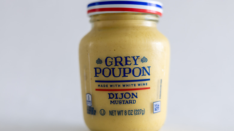 A jar of Grey Poupon mustard sits on a white table.