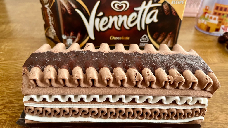 An unwrapped chocolate Viennetta sits on a wooden table with the box in the background.