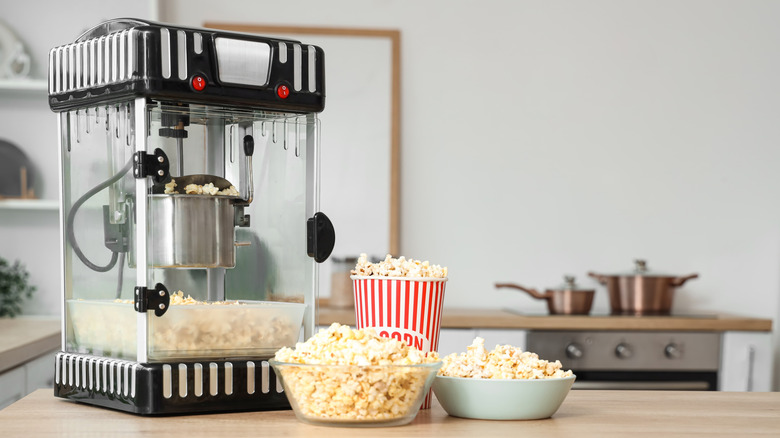 Popcorn maker on countertop behind bowl and bucket of popcorn