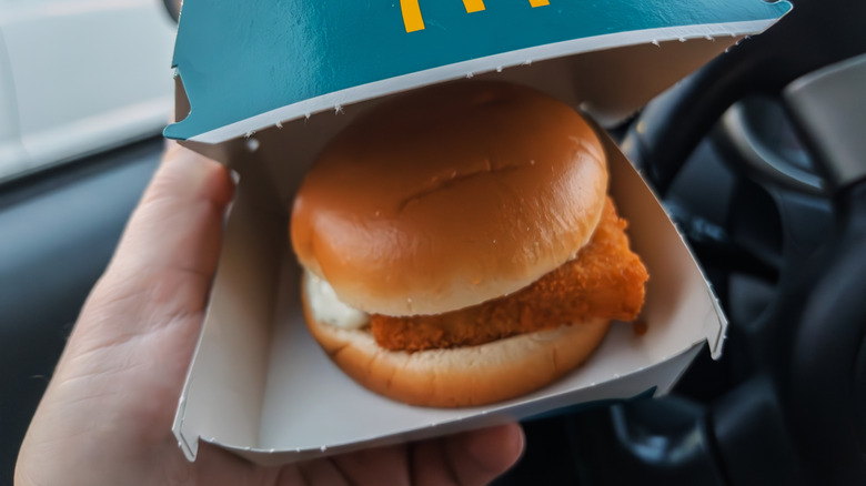Hand holding box of McDonald's Filet-O-Fish sandwich inside car