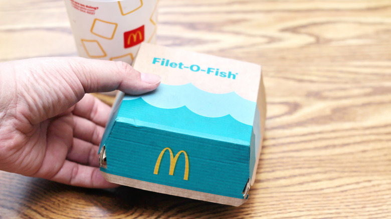 Hand holds Filet-O-Fish sandwich in closed cardboard container