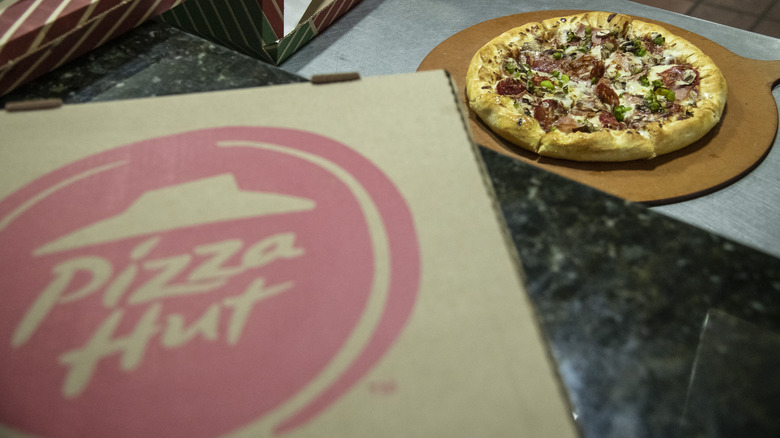 Pizza Hut box in the foreground with a meat and veggie pizza in the background