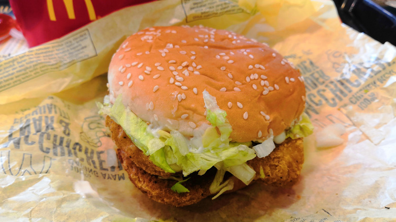 A Double-chicken burger from a McDonald's is unwrapped on a table with fries.