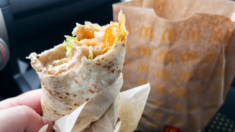 A hand holding a McDonald's Snack wrap that's half eaten in front of McDonald's to-go bacg