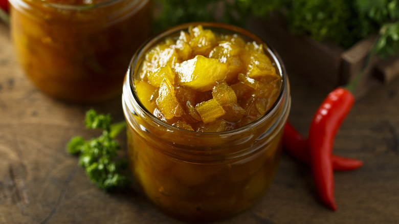 an open jar of mango and pear chutney with chilli peppers beside it