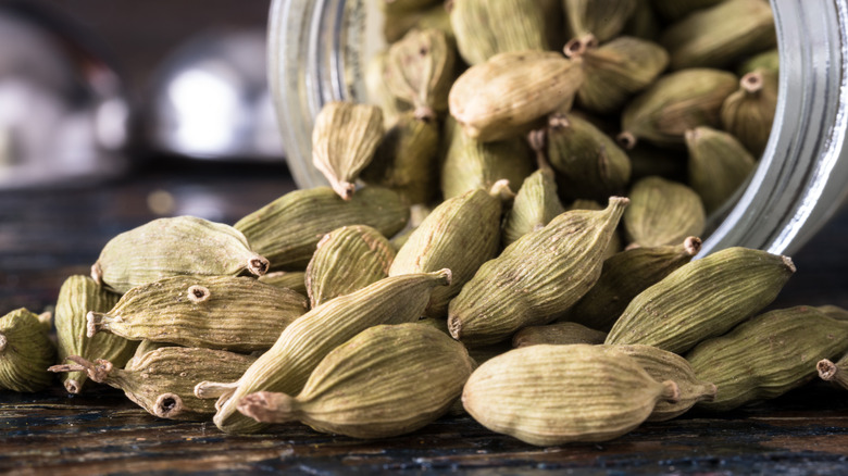 A close-up of loose green cardamom seed pods next to a jar.