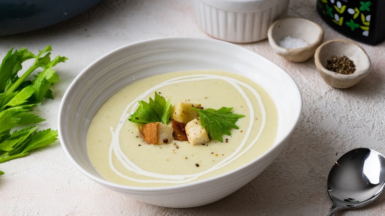 Cream of celery soup in white bowl with croutons and leafy garnish