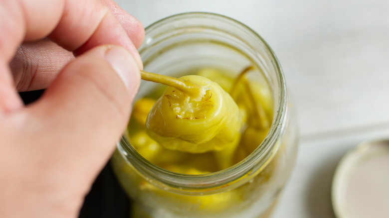 A person picks pepperoncini peppers out of a jar.