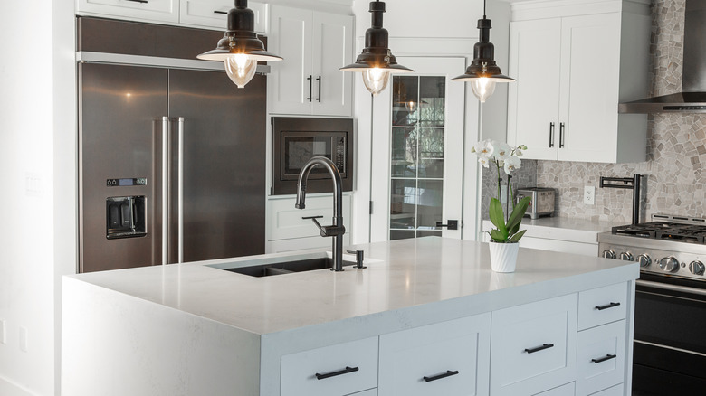 Modern kitchen with white countertop on an island, white cabinets, and pendant lights