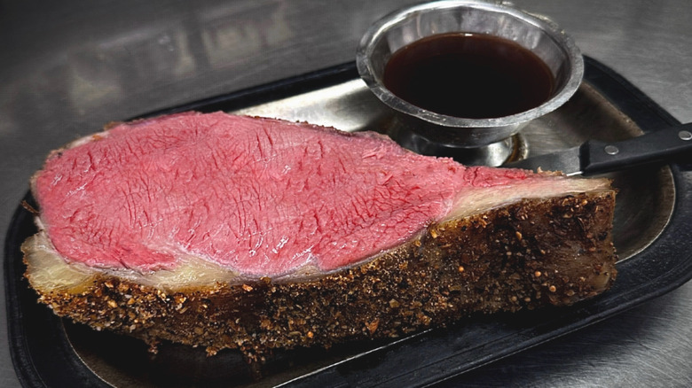 Prime rib with dark crust beside a bowl of sauce