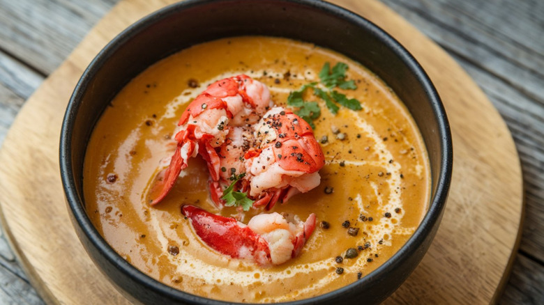 Bisque with cooked lobster in a bowl on a wooden serving board