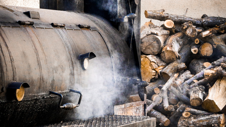 A barrel drum smoker next to a pile of chopped wood