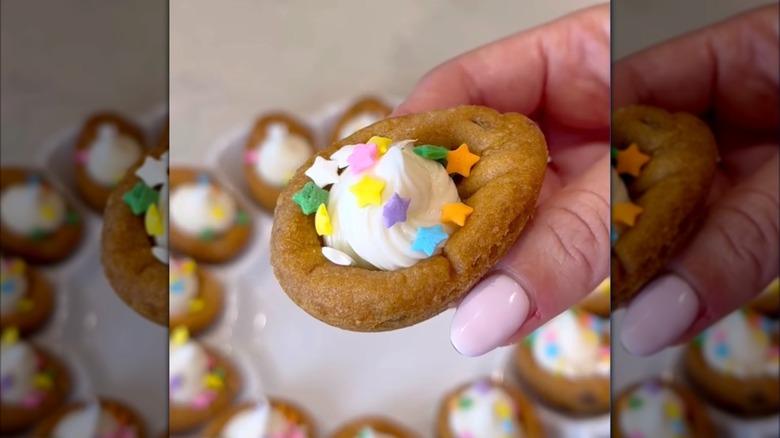 Hand holding cookie made to look like deviled egg filled with vanilla frosting and topped with star sprinkles