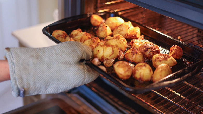 person using an oven mitt to place a baking pan of roasted potatoes in the oven