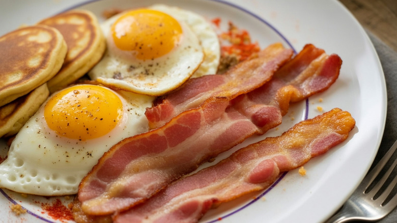 Diner breakfast plate with pancakes, fried eggs and bacon.