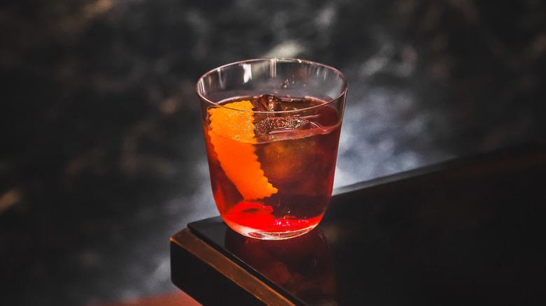 An Americano cocktail resting on a bar-top with a stone wall in the background