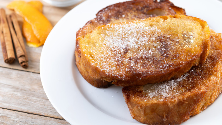 A beauty shot of thick French toast slices with cinnamon and white sugar on a white plate