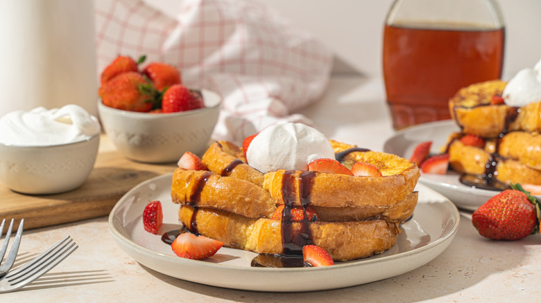 Two plates of French toast with strawberries, cream, and syrup